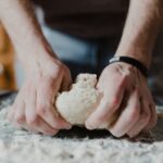 person holding white dough on brown wooden table