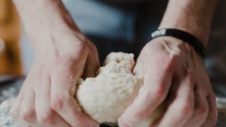 person holding white dough on brown wooden table