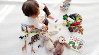 boy sitting on white cloth surrounded by toys