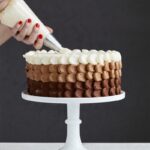 person holding white ice cream cone with brown and white round cake