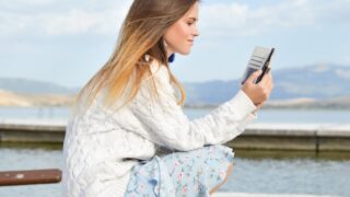 woman using smartphone while sitting of dock during daytime